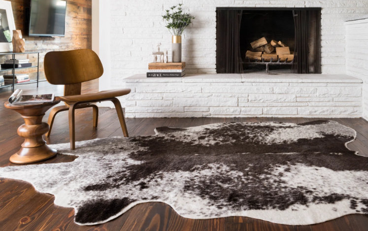 black-and-white cowhide rug in modern living room with wood furniture and white brick fireplace