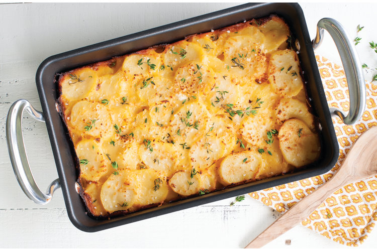 Rectangular cast iron roasting pan with stainless steel handles and filled with au gratin potatoes.