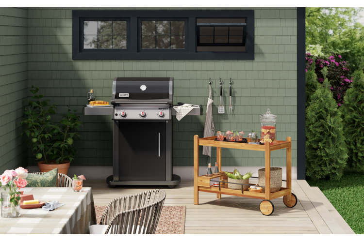 A patio with a weber grill beside a wood patio serving cart used as a drink station.