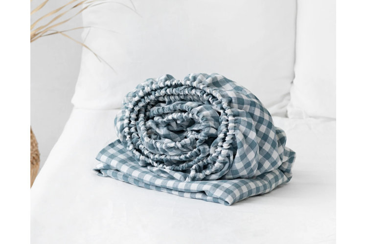 blue and white checked fitted sheet rolled up and placed on a bed with white linens