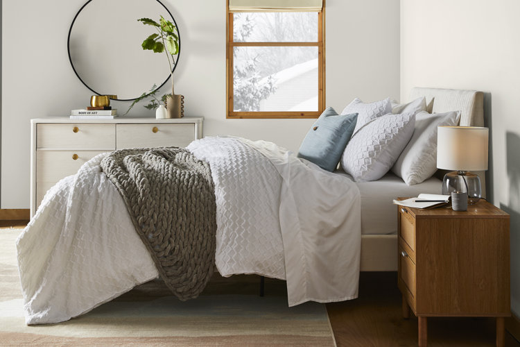 gray upholstered bed with light gray sheets and a white duvet cover