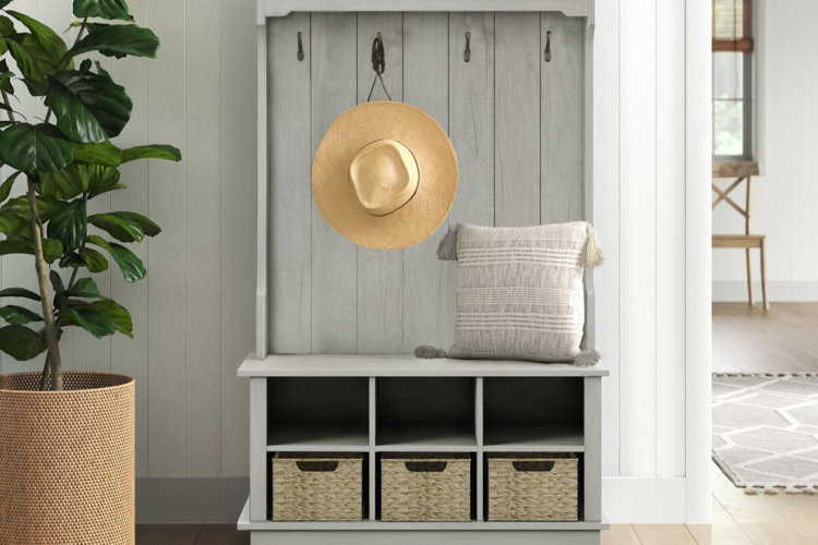 light gray hall tree with bench, cubby storage baskets and wall hooks styled beside a potted plant in a bright entryway