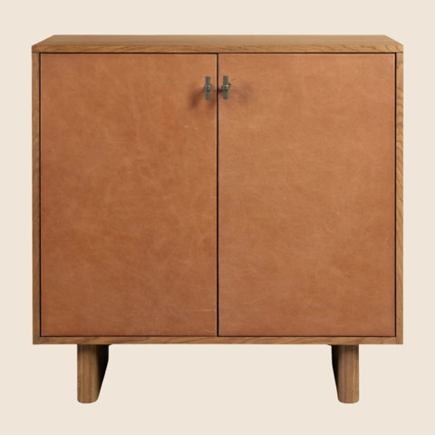 Mid-century modern accent cabinet with a wood frame and tan leather-wrapped double doors featuring minimalist metal hardware.