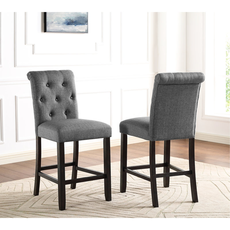 Tabouret de 2 comptoirs en bois massif gris. Sièges et dossiers rembourrés et à boutons. Pieds en bois avec finition. Chaises à haut dossier avec courbe élégante. L 23 po x P 19 po H 39,19 po. Largeur du siège 19 po, 25 po, profondeur 16,5 po. Certains