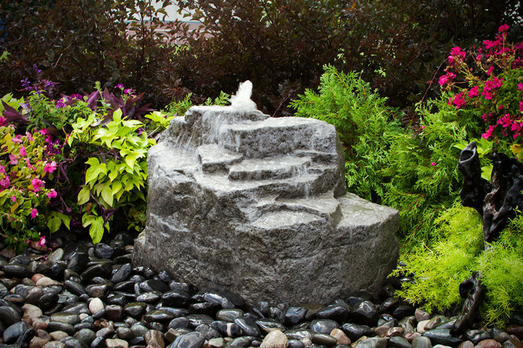 large rock-look water feature in a beautiful flower garden