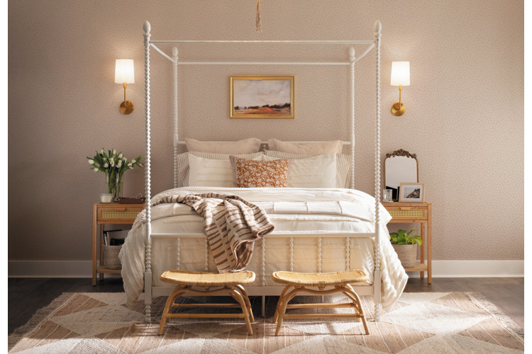 Monochrome bedroom with beige patterned wallpaper, a white canopy bed with beige bedding, and a diamond pattern beige rug.