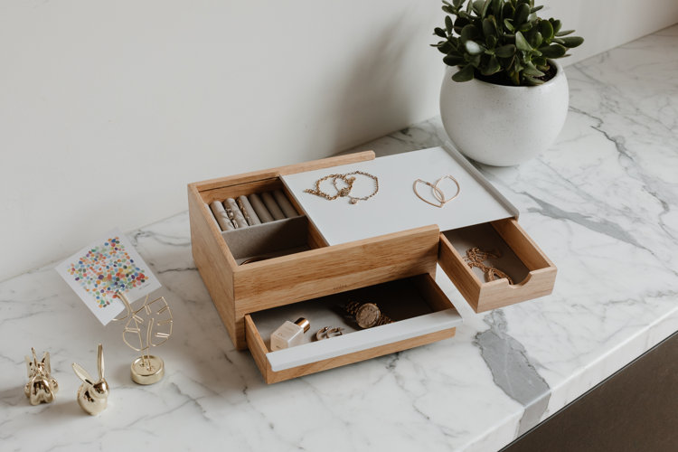 Light wood jewelry box filled with gold jewelry on a marble counter