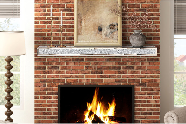 brick fireplace with silver mantel shelf decorated with gold candlesticks, framed artwork, and a gray vase with branches