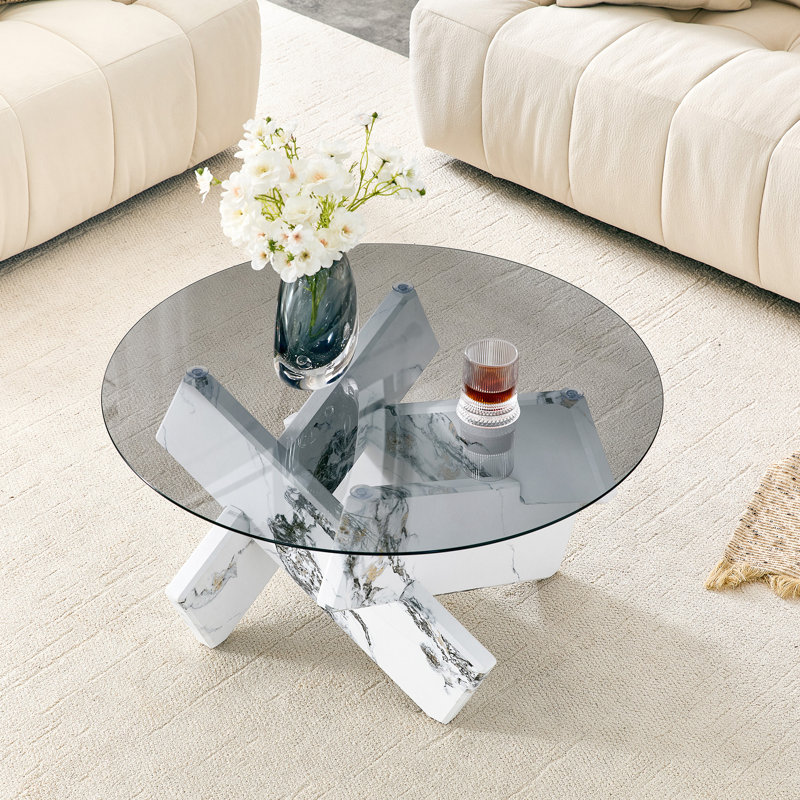 Table basse ronde en forme de X, de style artistique, avec piètement à motif de marbre et dessus en verre trempé.