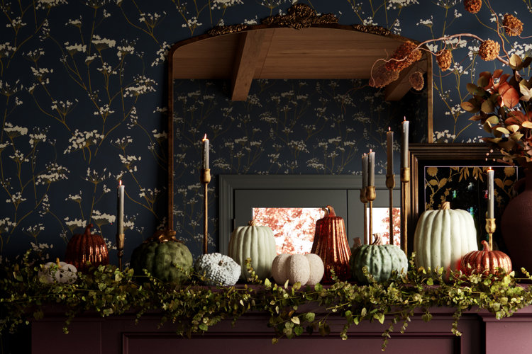 A fireplace mantel with white, light green, and copper decorative pumpkins paired with green foliage and gold candlesticks.