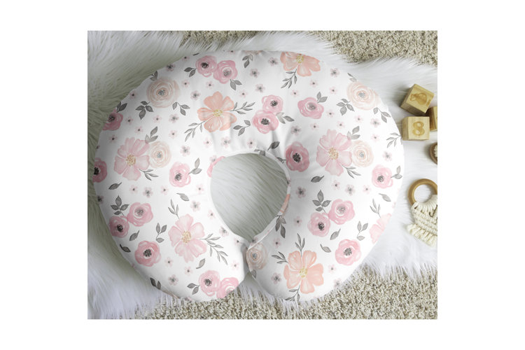 A c-shaped pink floral nursing pillow on a white faux fur rug beside wooden blocks and toys.