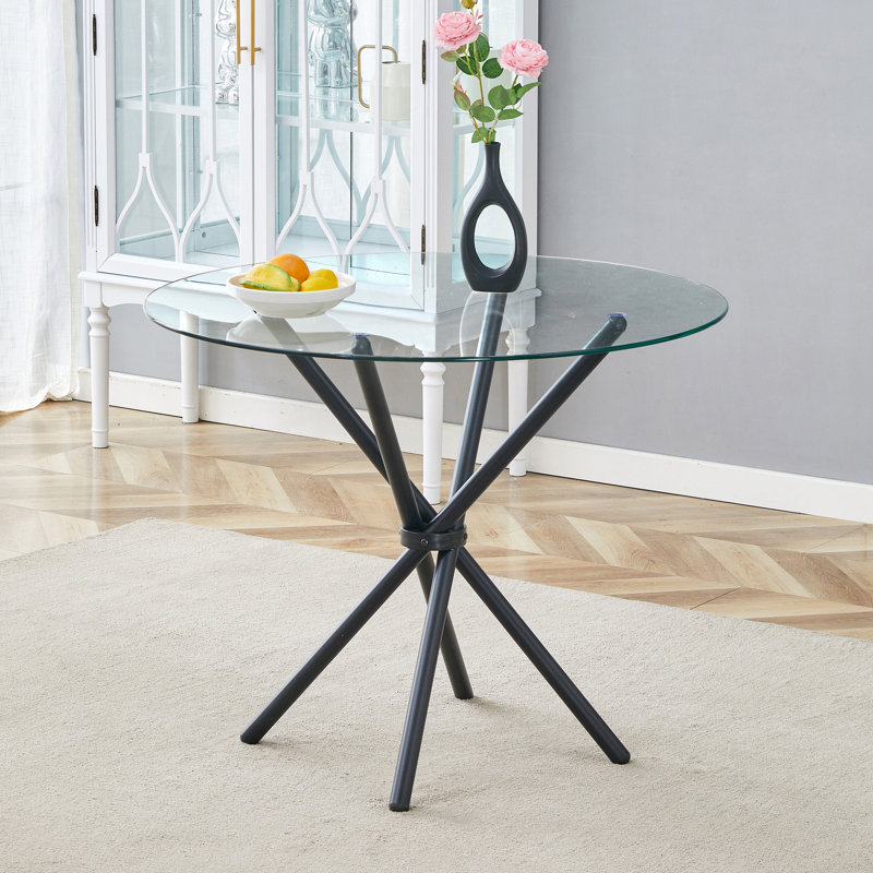 Table circulaire en verre trempé transparent avec pieds en métal noir entrelacés pour les espaces minimalistes modernes.