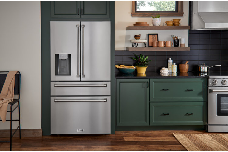 stainless steel fridge in a kitchen with green cabinets and black subway tile