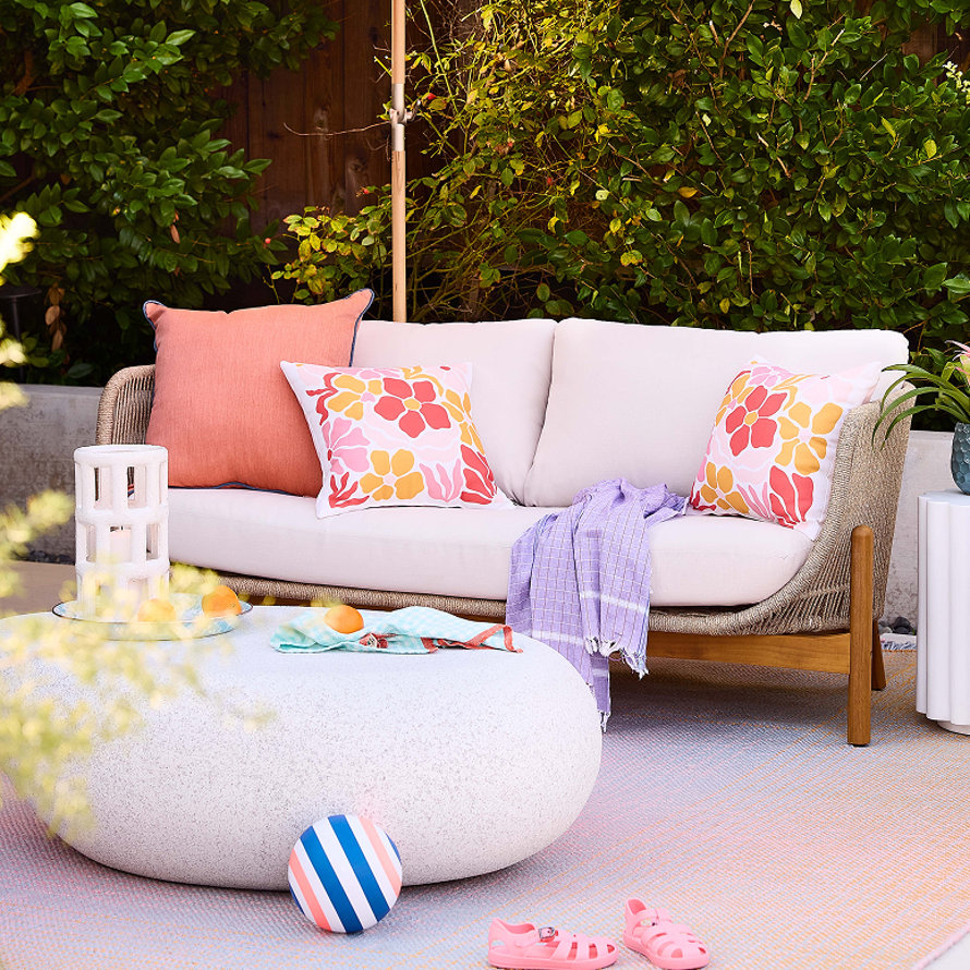 Terrasse extérieure avec un canapé blanc, des coussins, une table basse ronde en béton et des sandales d'enfant.