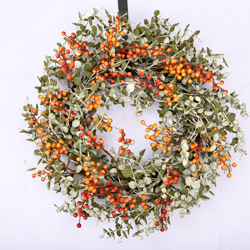 A wreath with green leaves and orange and red berries