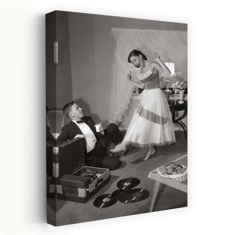 1950S 1960S Teen Couple In Living Room In Prom Dress & Tuxedo Guy Sitting On Floor & Girl Dancing To Music From A Record Player Romantic Contempora...
