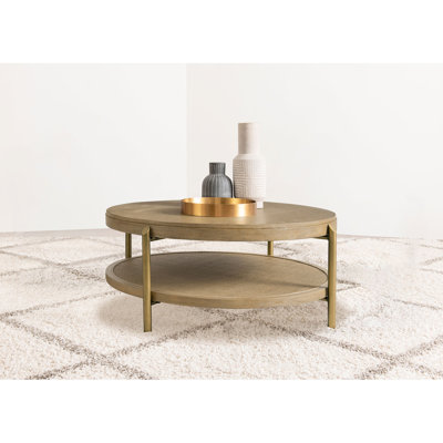 Table basse ronde en laiton vieilli, fini sablé, étagère de rangement ouverte, placage en frêne, pieds naturels, idéale pour le salon ou la détente.