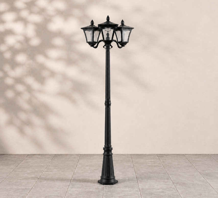Traditional three-head black outdoor lamp post with glass panels standing on a tiled patio.