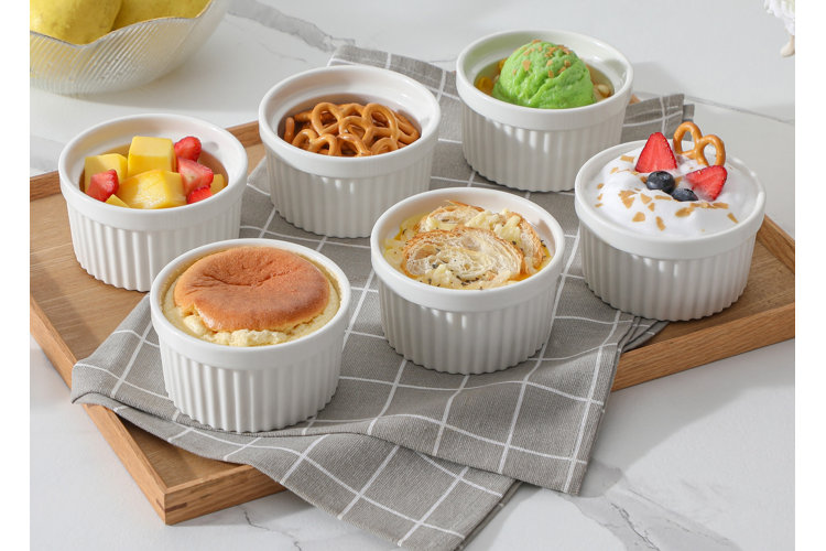 what is a ramekin set of six white ramekins with fruit, pretzels, ice cream, souffle, mac and cheese, and yogurt in them on a wood cutting board