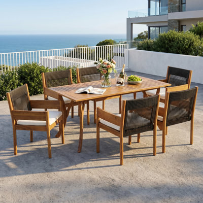 Ensemble de salle à manger d'extérieur Celia pour 6 personnes, style côtier moderne, en bois d'acacia, avec chaises à accoudoirs tressés, coussins et table à lattes à pieds incurvés.