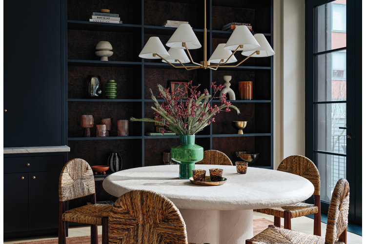 Dining room with black built-in shelves behind a white pedestal dining table with a green vase and flower arrangement.