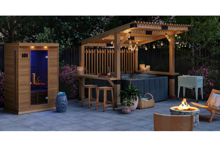 Patio with a square hot tub underneath a wooden pergola with string lights and beside a fire pit and a wooden sauna.