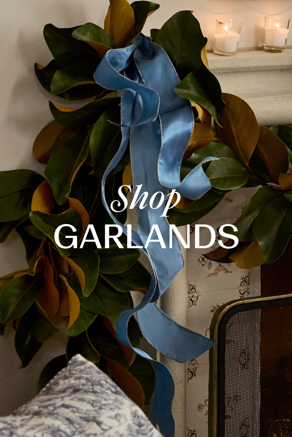 Shop GARLANDS with a decorative blue ribbon draped over a magnolia leaf garland on a fireplace mantel.