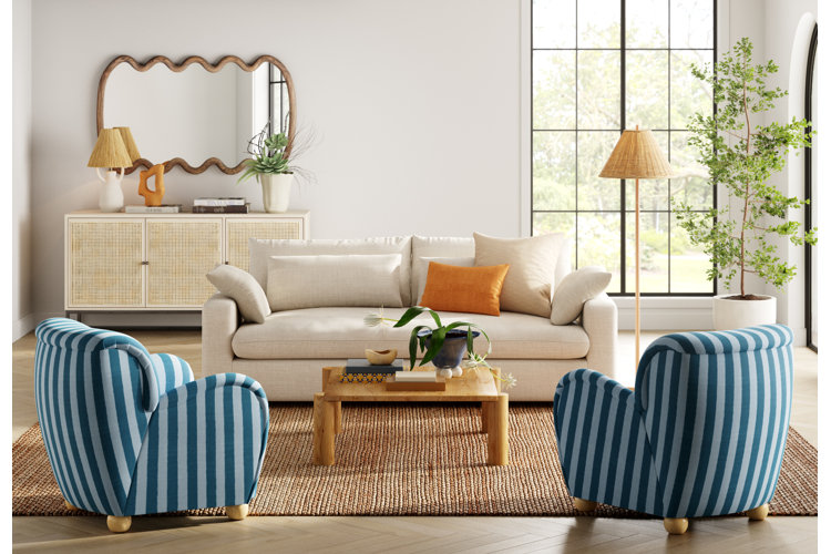 long living room with a white sofa and two blue striped accent chairs with a long hanging wall mirror