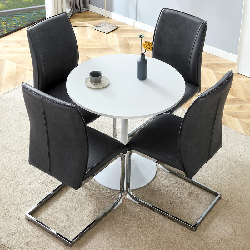 Ensemble de table et de chaises. Petite table ronde stable en forme de verre - 31,9 po x 31,9 po avec 4 chaises en polyuréthane foncé doux et confortable avec un pied en métal argenté arqué. Créez votre espace exclusif de luxe discret.