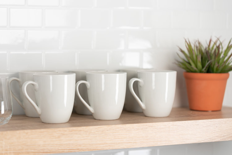 six white coffee mugs and a potted plant on a light wood floating shelf