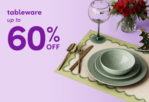 Tableware up to 60 percent off, featuring a holiday-themed place setting with a green scalloped placemat, speckled dinnerware, gold flatware, and a Christmas wine glass.