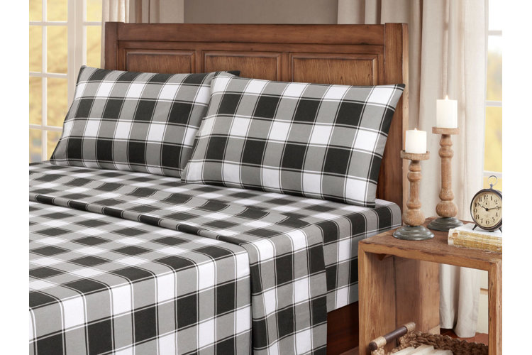 black and white gingham duvet cover on a large wood bed next to a wood nightstand holding two wood candle holders and an alarm clock