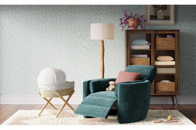 Beautiful nursery with a woven bassinet next to a blue velvet recliner with a red throw pillow. White floor lamp with a white area rug next to a linen cabinet