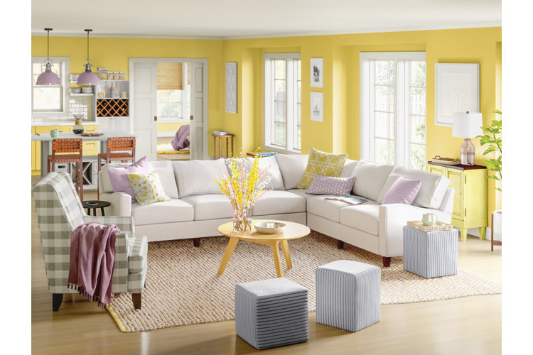 Living room with yellow walls, a white sectional sofa, and yellow and purple throw pillows.