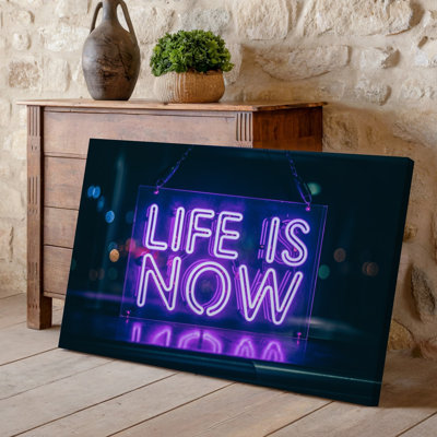Canvas A Vibrant Neon Sign Displaying The Phrase LIFE IS NOW Wall Art In Bold Glowing Purple Letters Hanging Against A Dark Reflective Canvas Wall Art