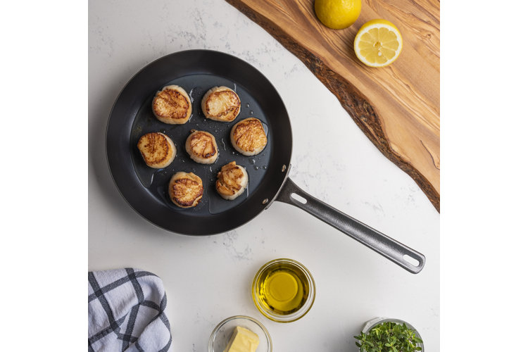 Cast iron frying pan with seared scallops beside small bowls filled with olive oil, butter, and herbs.