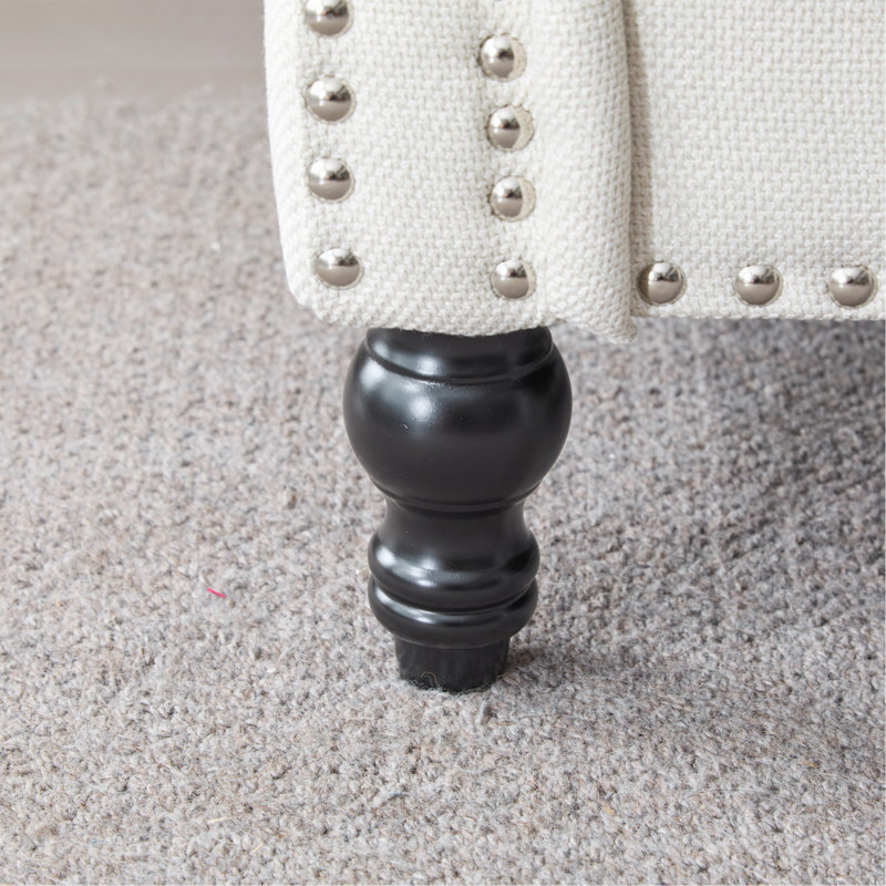 Canapé traditionnel en similicuir beige, profondeur d'assise de 56 cm, accoudoirs arrondis, pieds en bois et garniture cloutée.