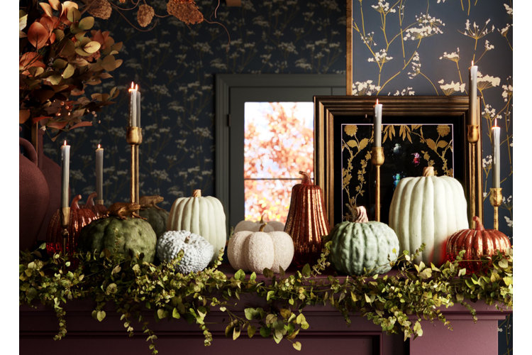 Close up of a living room mantle with a green foliage garland, gold candlesticks and taper candles, and faux pumpkins.