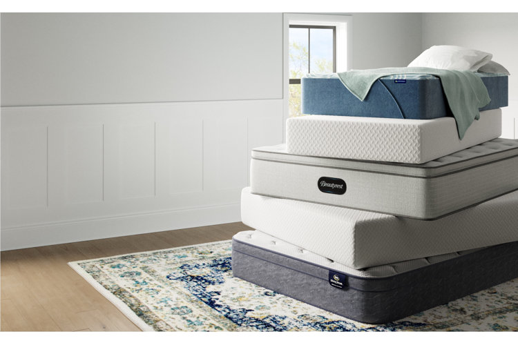 Stack of mattresses demonstrating the mattress firmness scale in a room with white wall paneling and an oriental rug