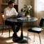 Une table de salle à manger ronde de style luxueux et noire, équipée d'une élégante base en métal en forme de tulipe et d'un plateau en panneau de fibres à densité moyenne de 31,5 pouces, présente un style médiéval moderne dans son ensemble. It