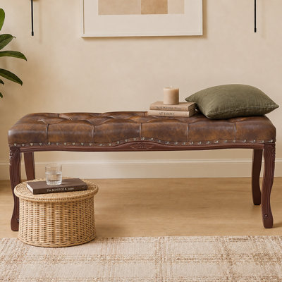 Banc capitonné de style années 50, large de 115 cm, à placer au pied du lit. Revêtement en similicuir beige, finitions cloutées et pieds en bois massif sculpté.