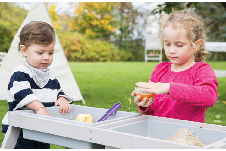 two children playing with a tabletop sandbox outside in the yard
