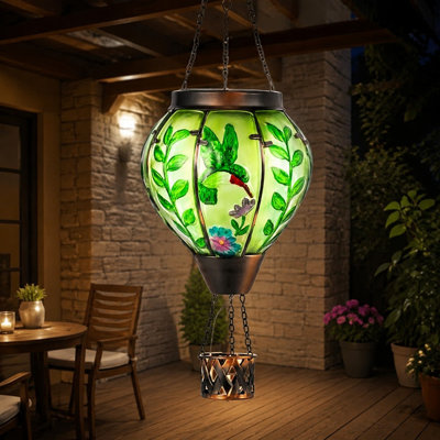A Green hot-air-balloon solar lantern is Handmade from Glass with a flame effect and waterproof construction for decorative outdoor use on patios, in gardens, or on porches.