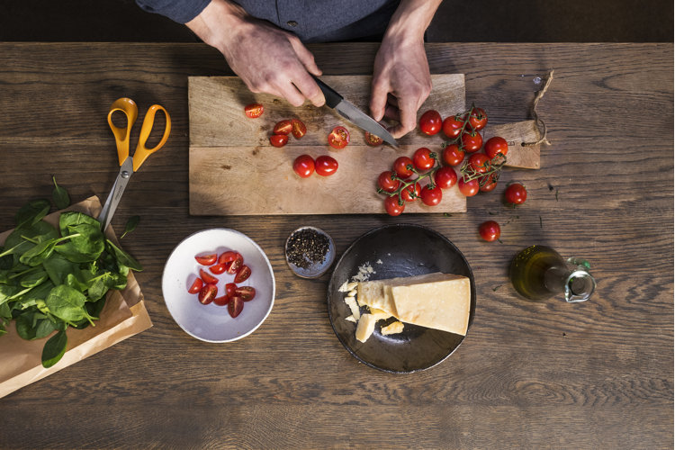 aerial view of a person using a paring knife to slice tomatoes