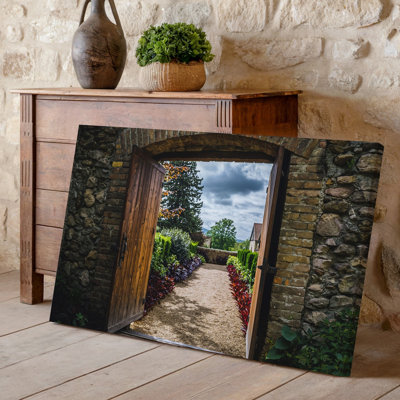 Toile, porte en bois rustique, Ajar dans une arche de pierre, art mural encadré par des briques patinées révélant un sentier de jardin serein
