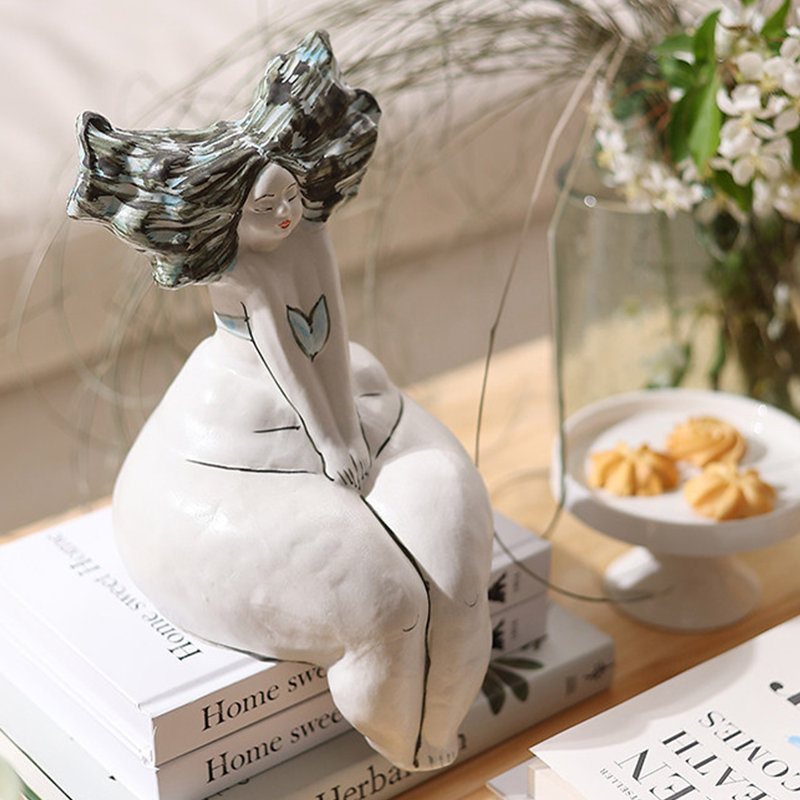 Objet décoratif en céramique représentant une femme assise aux courbes blanches