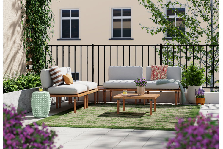 Apartment balcony with a modular outdoor sectional, green outdoor rug, and garden stool styled for small-space outdoor lounging