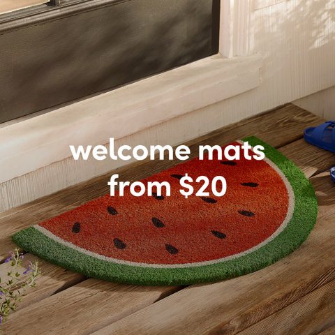 A semi-circle coir doormat designed to look like a red watermelon slice on a wooden porch from $20.