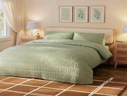 A serene bedroom featuring a bed with sage green textured bedding, rattan nightstands, and botanical prints on the wall