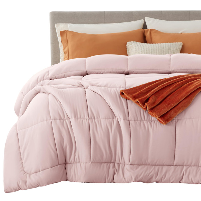 Dusty pink box-stitched comforter on a bed with a beige headboard.